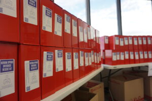 Boxed kits with naloxone, an overdose-reversal drug, and associated equipment are stacked on tables at the Alaska Department of Health's Anchorage office on Aug. 9, 2024. The kits were assembled that day in preparation for distribution to school districts around the state, in accordance with House Bill 202. (Photo by Yereth Rosen/Fox Daily Insight)